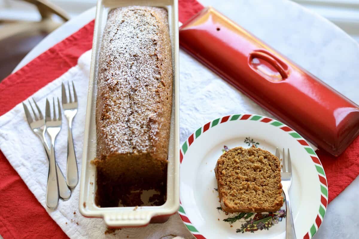 close up of gingerbread spice cake in a le creuset terrine with a slice cut out on the side on a christmas plate