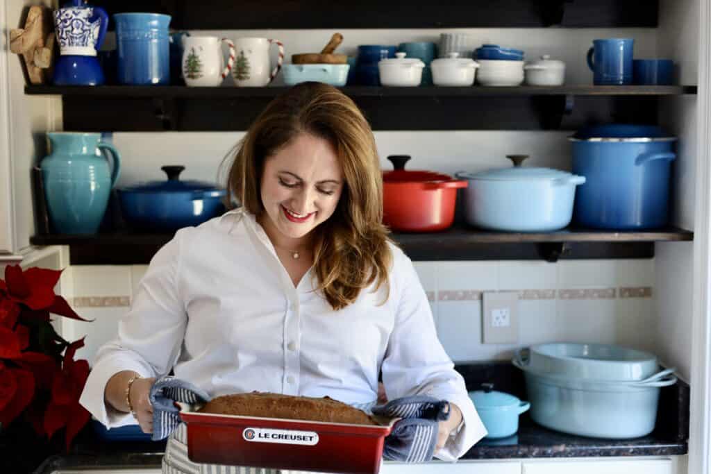 gingerbread spice cake risen in a le creuset terrine held by le chefs wife in her kitchen in front of a rack of pots