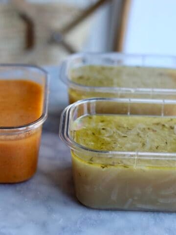 3 freezer containers with French onion soup and vegetable soup inside on a table