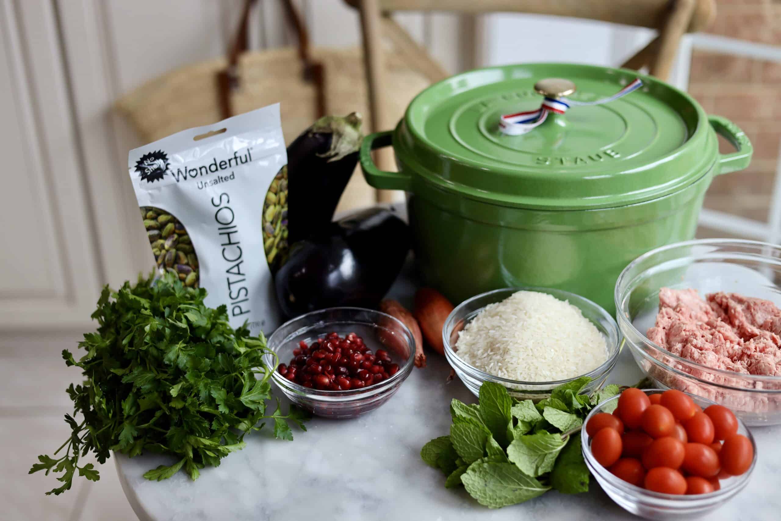 ingredients for eggplant, pistachio, ground lamb, and pomegranate seed rice next to the dutch oven to cook them in