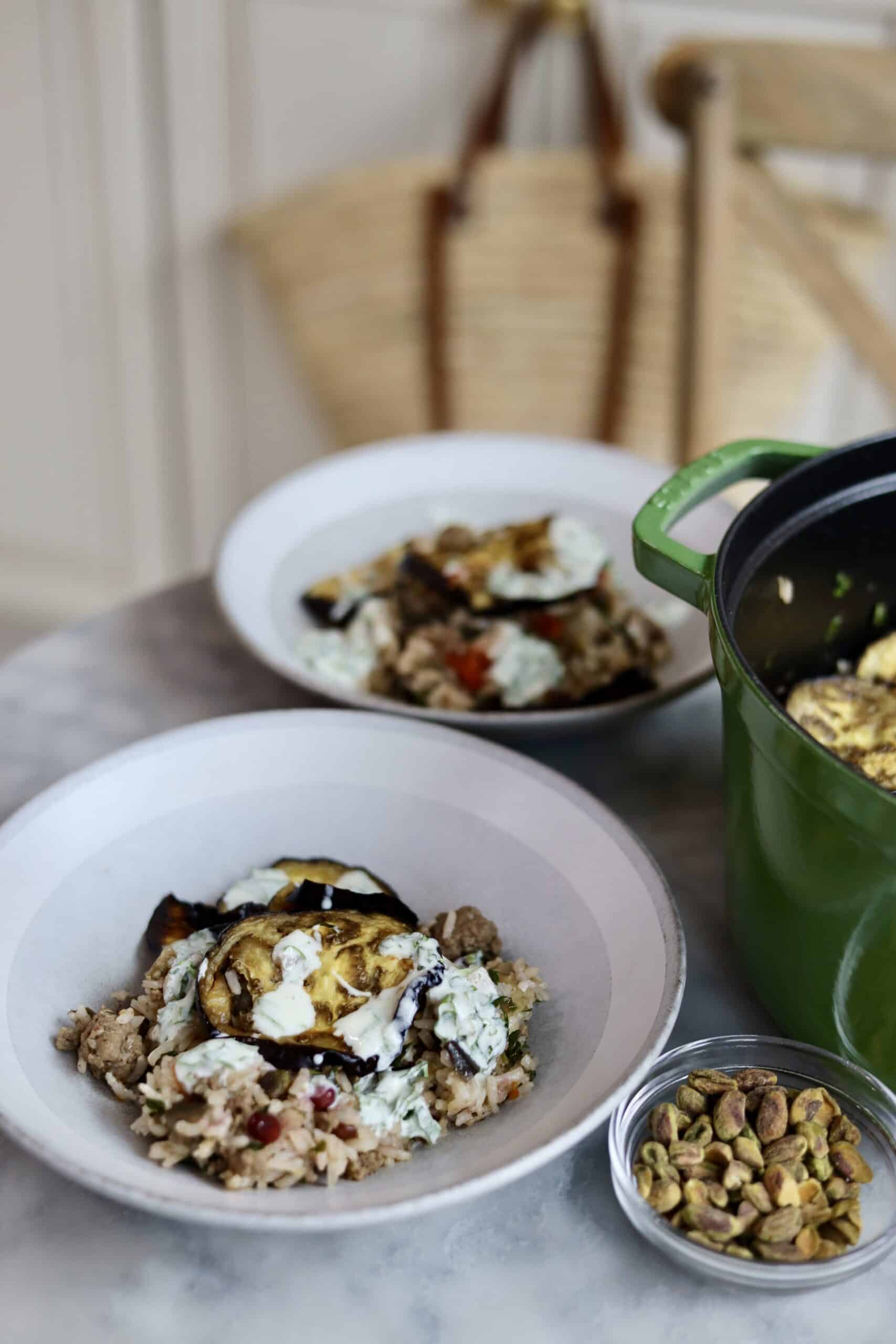 eggplant, pistachio, ground lamb, and pomegranate seed rice in a bowl with yogurt sauce next to the dutch oven it was cooked in