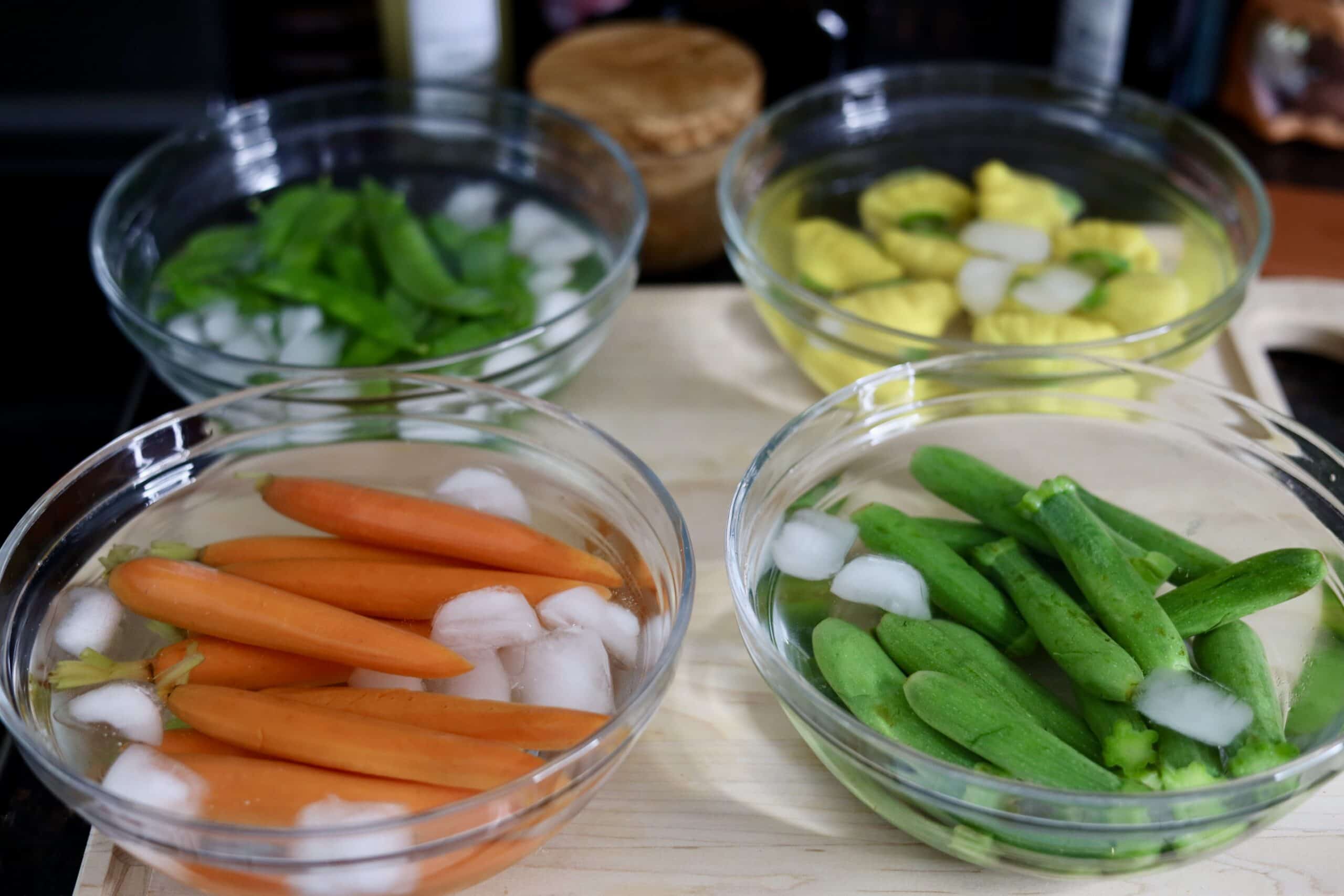 carrots, zucchini, spring peas and patty pan squash in bowls of ice water for blanching vegetables