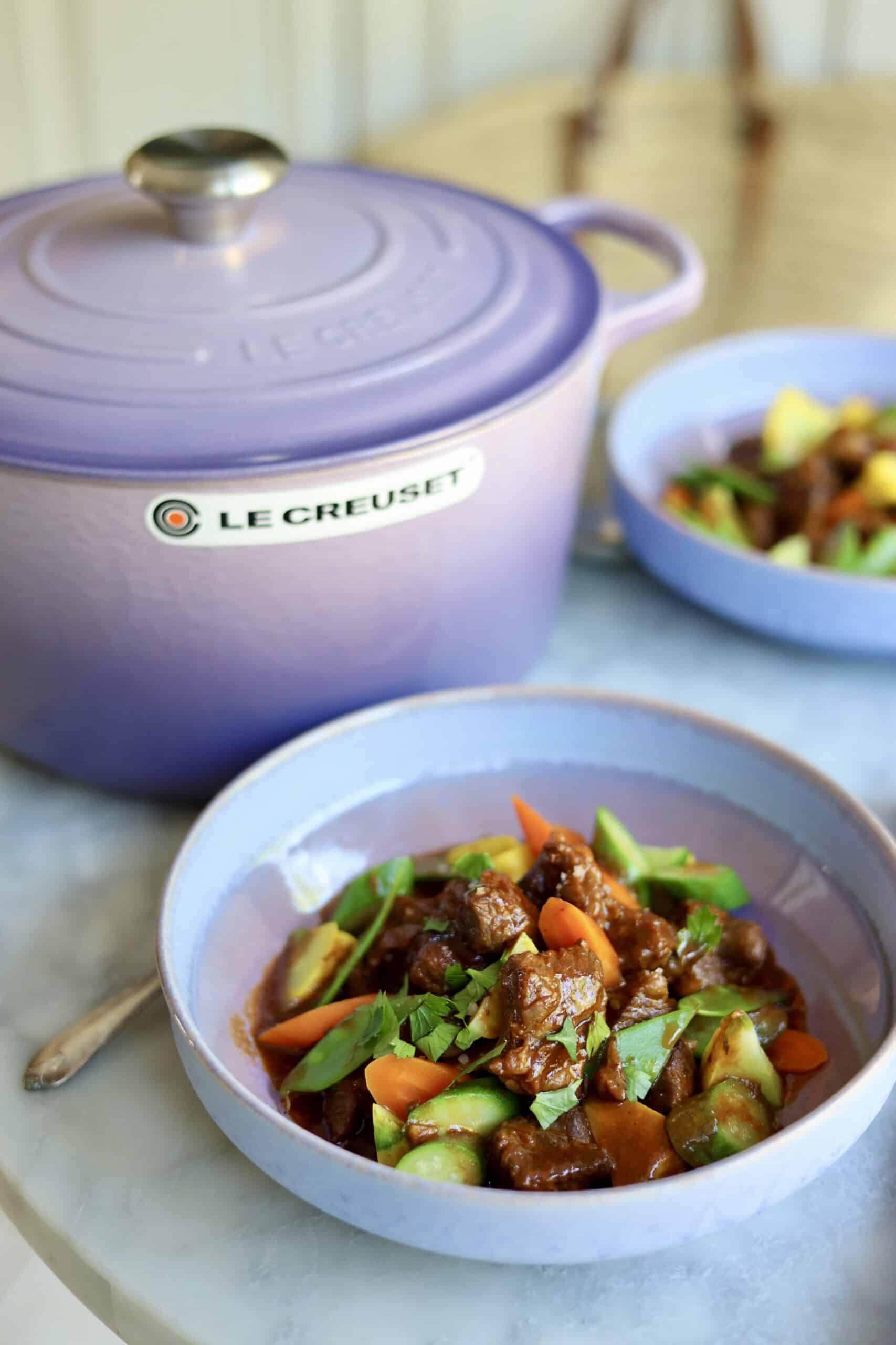 Navarin d'agneau lamb stew in a stoneware dish next to a provence purple le creuset dutch oven