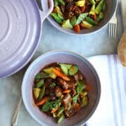 Navarin d'agneau lamb stew in a stoneware dish next to a provence purple le creuset dutch oven next to a baguette