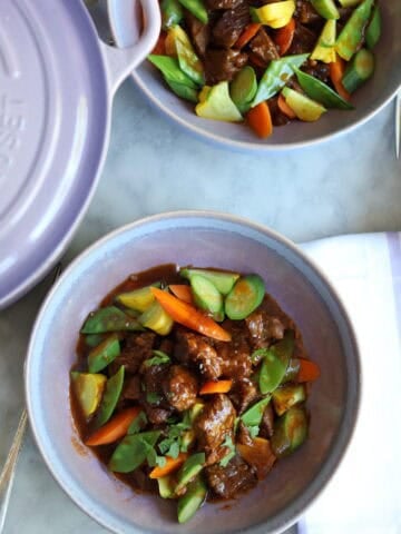 Navarin d'agneau lamb stew in a stoneware dish next to a provence purple le creuset dutch oven next to a baguette