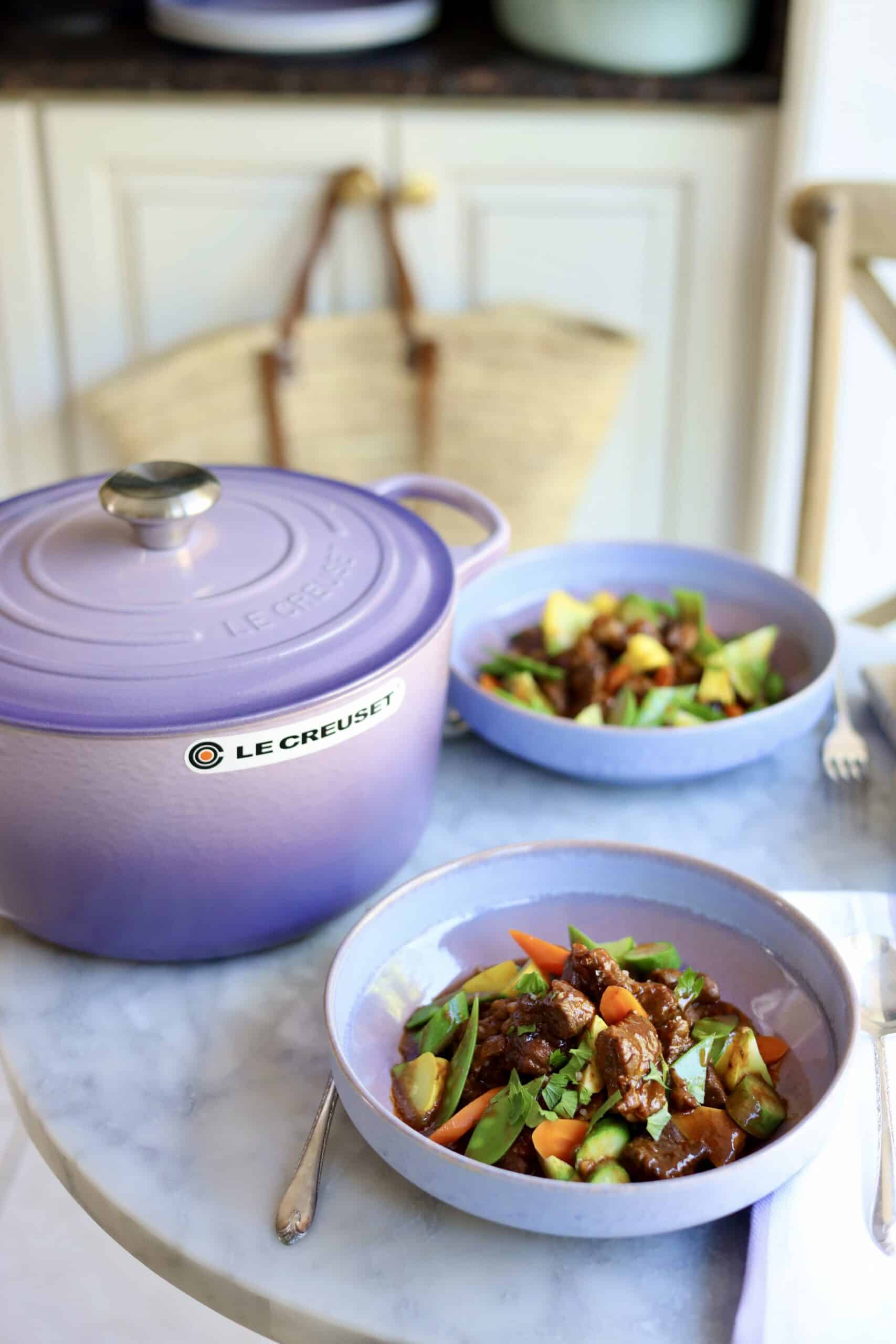 Navarin d'agneau lamb stew in a stoneware dish next to a provence purple le creuset dutch oven