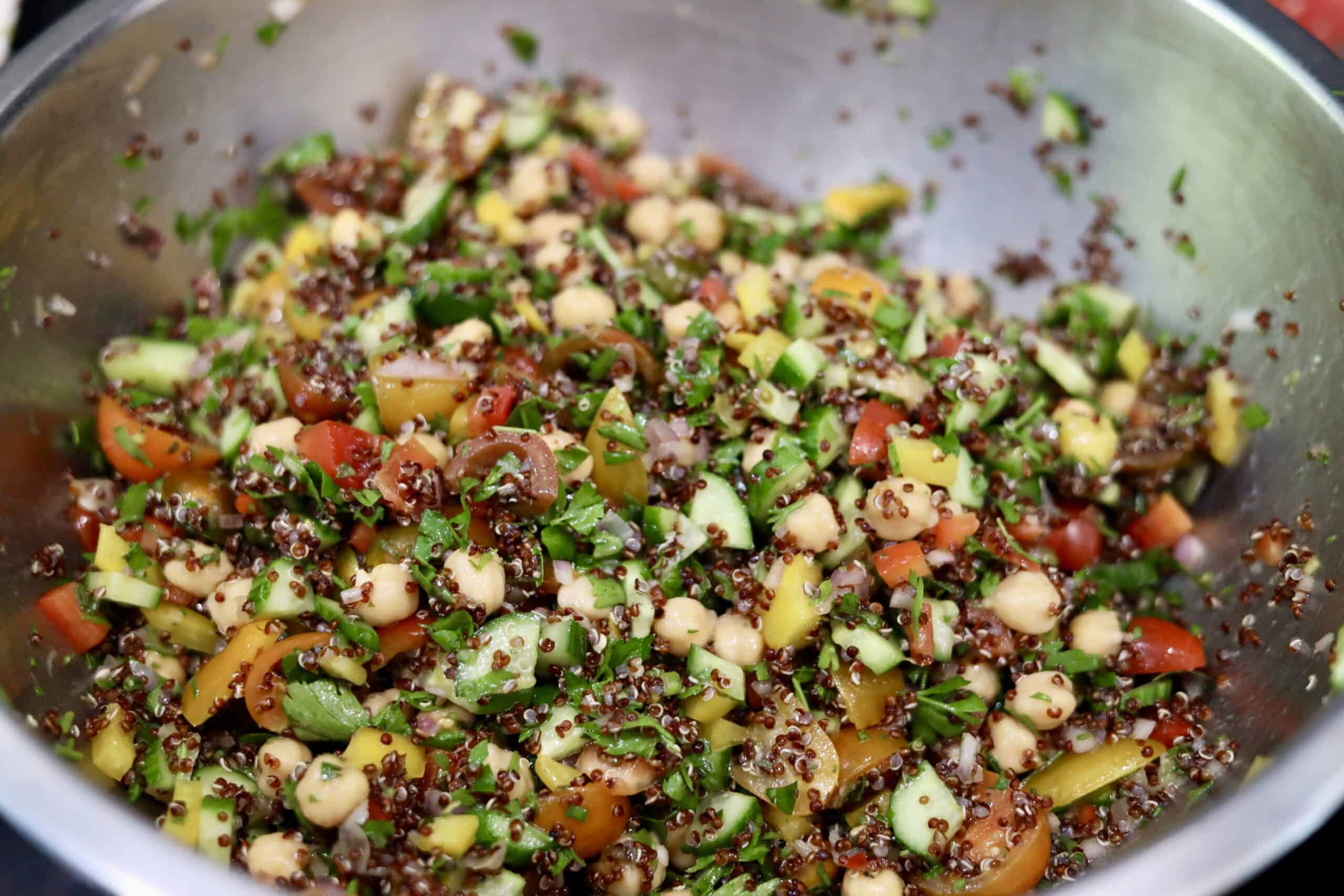 gluten-free quinoa tabbouleh with cucumbers, peppers and chick peas in a stainless steel mixing bowl