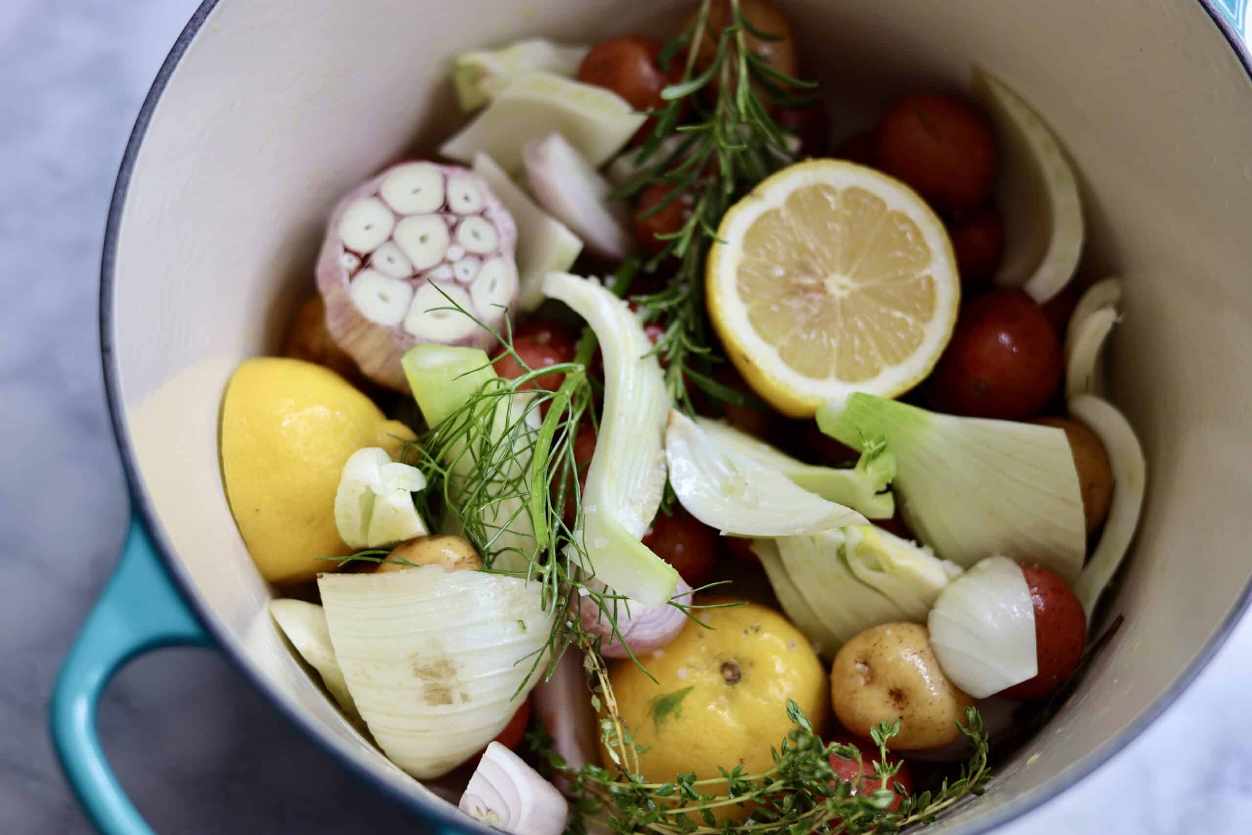 French Riviera Roast Chicken Ingredients in a dutch oven - potatoes, fennel, herbs, lemon, garlic