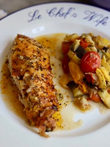 Provencal roast chicken ratatouille on a plate - the chopped vegetables and herbs for the ratatouille on the bottom - fresh out of the oven- the skin is crispy. The dutch oven is in the background