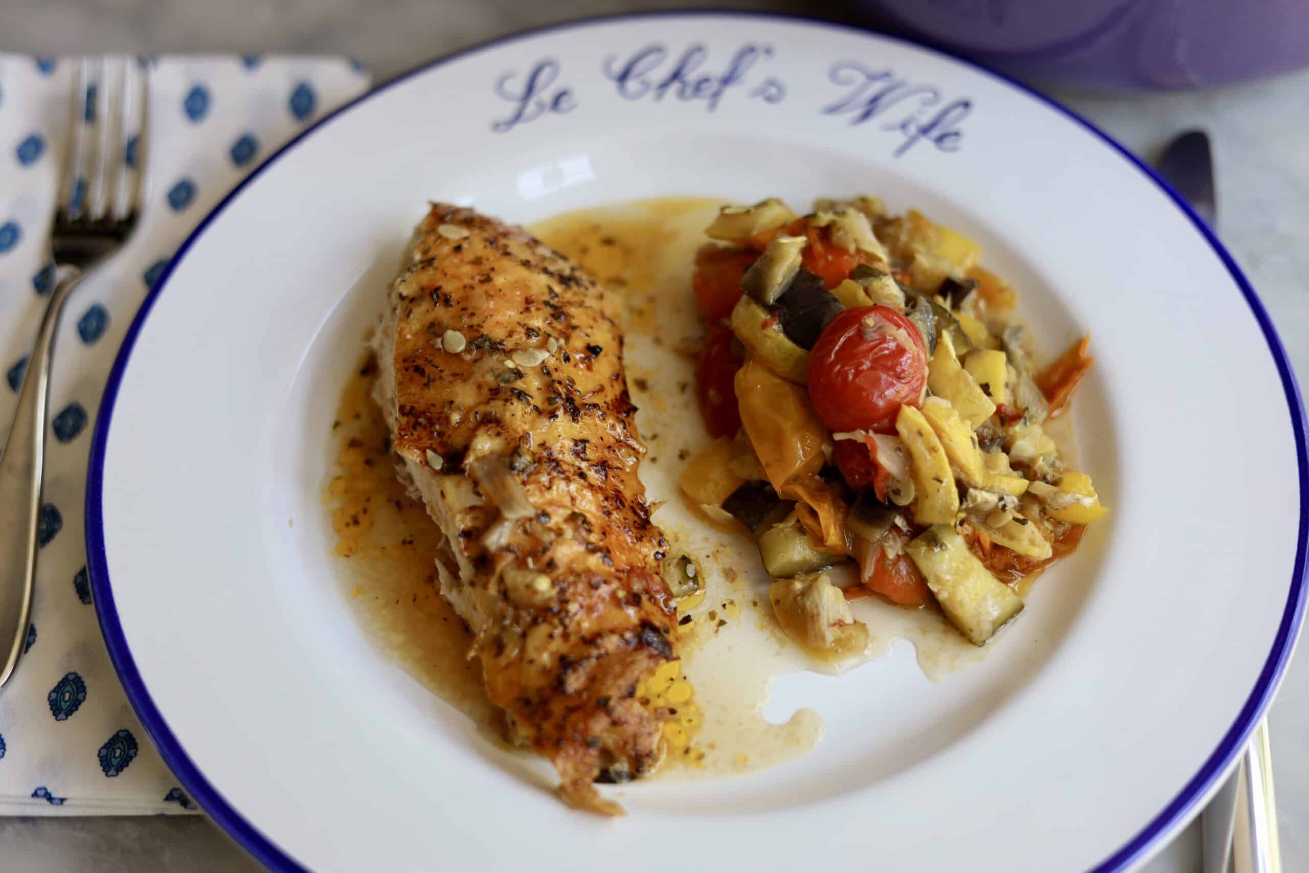 Provencal roast chicken ratatouille on a plate - the chopped vegetables and herbs for the ratatouille on the bottom - fresh out of the oven- the skin is crispy. The dutch oven is in the background