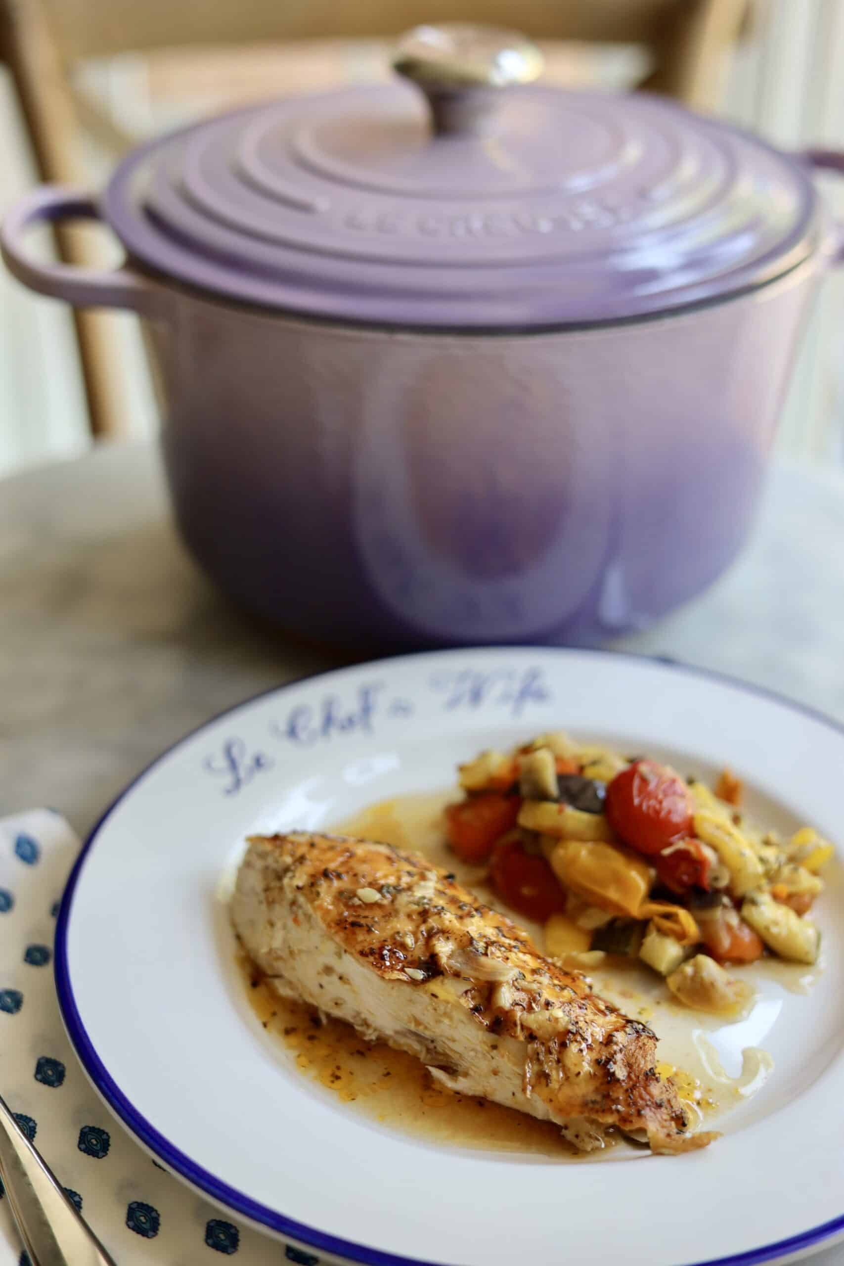 Provencal roast chicken ratatouille on a plate - the chopped vegetables and herbs for the ratatouille on the bottom - fresh out of the oven- the skin is crispy. The dutch oven is in the background
