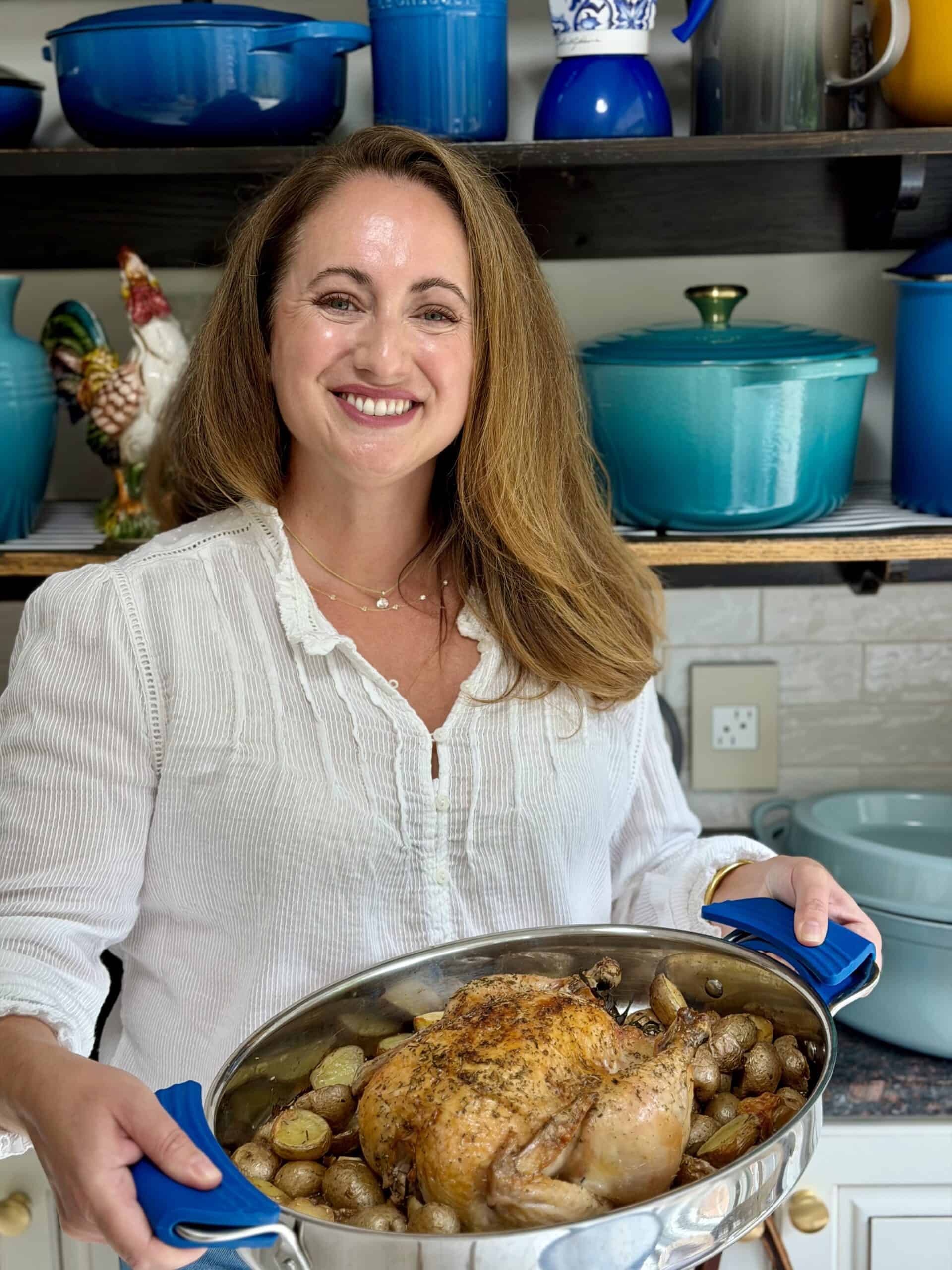 Anina Belle Giannini standing with a roast chicken in her kitchen in front of her wall of dutch ovens